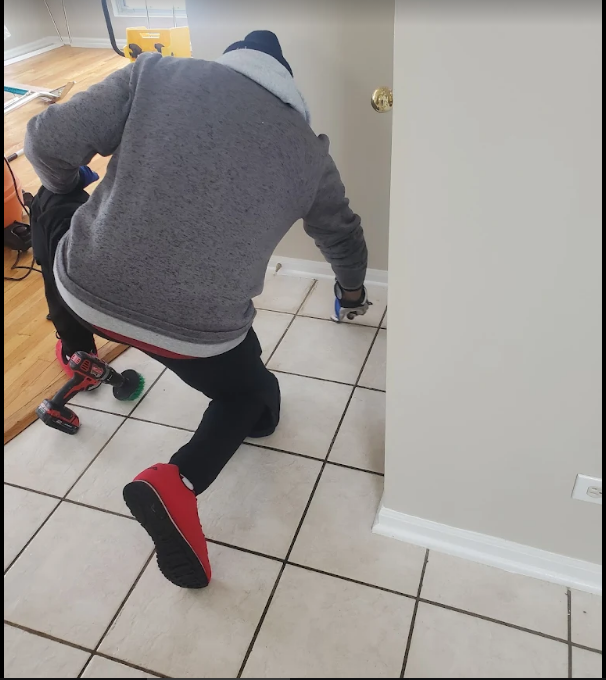 Crew member detailing grout lines on a tile floor by hand